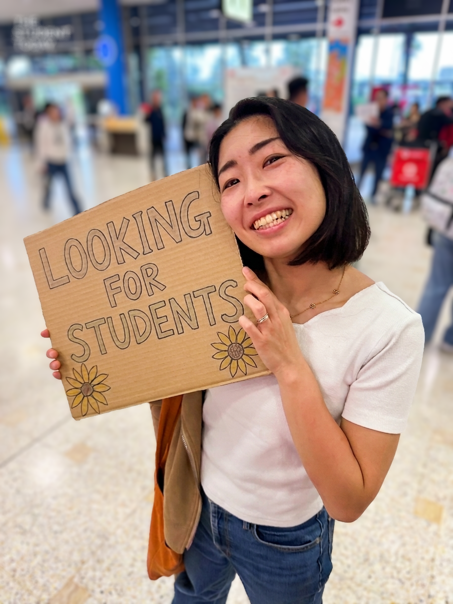 Mai smiling and holding a handmade sign that says Looking for students